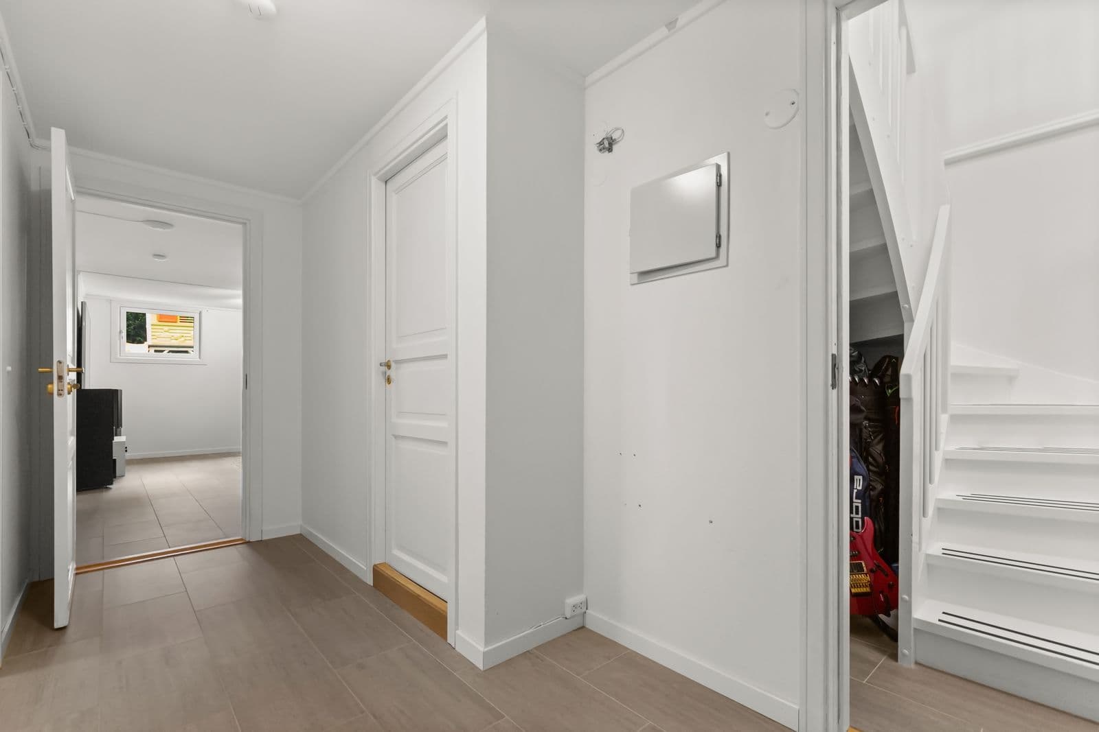 A bright white hallway with a staircase and open doors