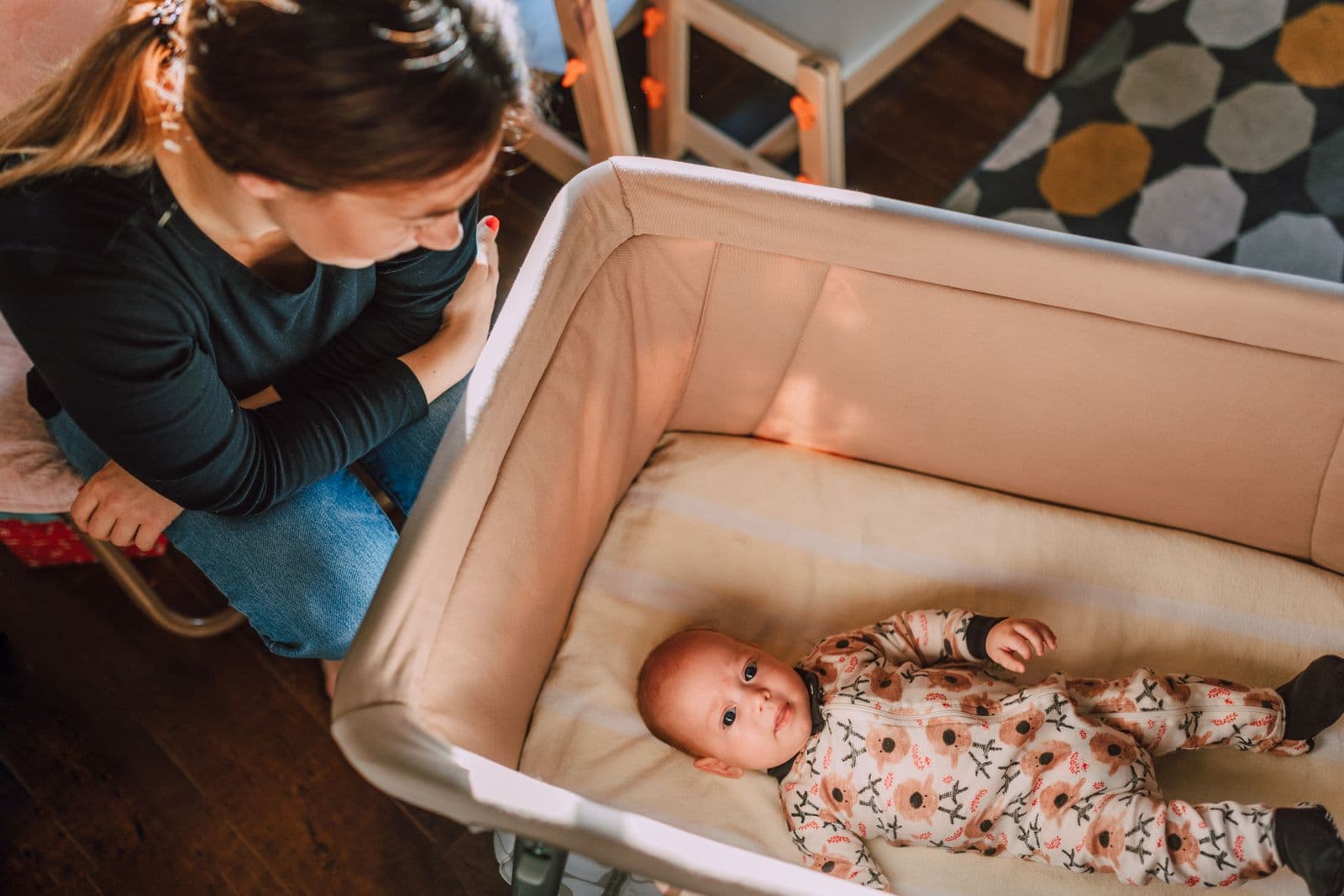 A parent kneeling beside a bedside bassinet with a baby lying in it