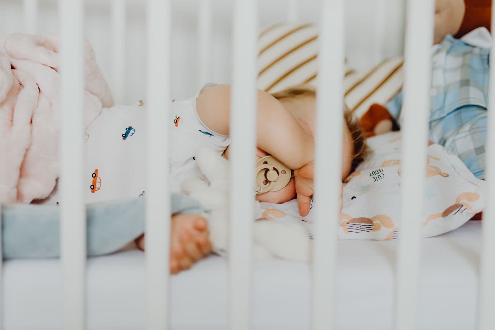 A baby asleep in a crib with a pacifier, seen from the side