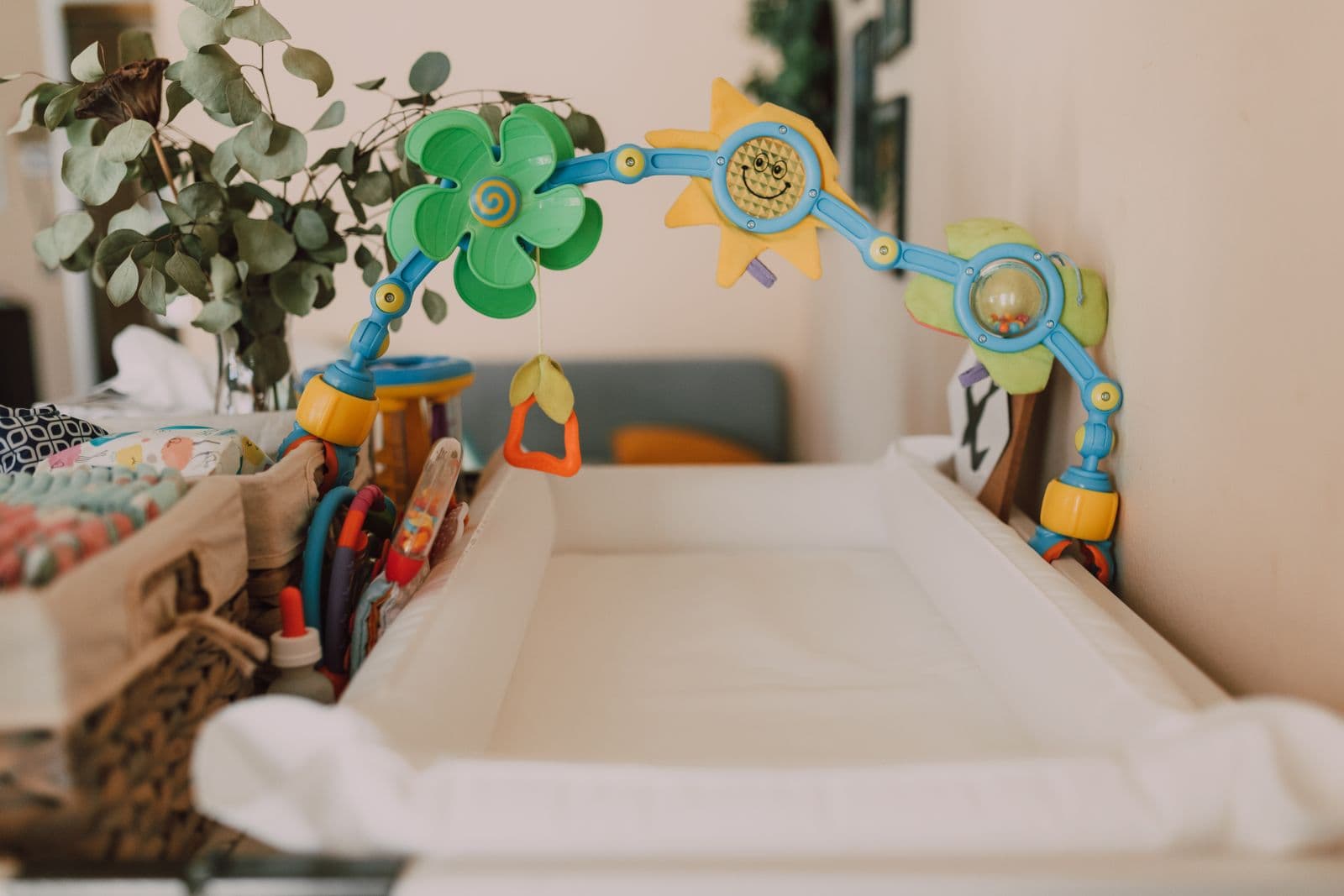 A contoured changing pad on a nursery changing table with a toy arch and a basket of diapers and supplies beside it