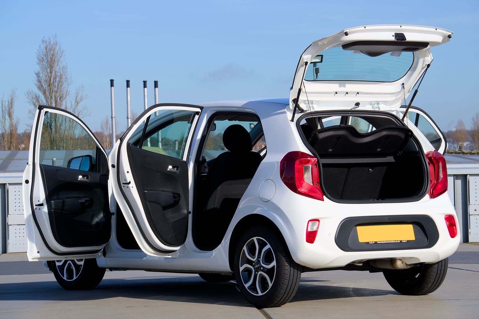 A small white city car photographed with both passenger doors and the hatch open, showing a shallow rear bench