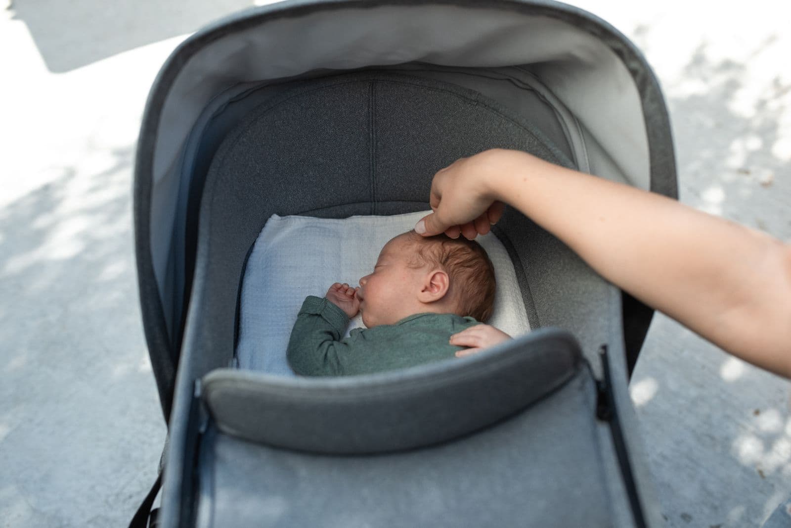 A newborn asleep in a stroller bassinet while a parent reaches in