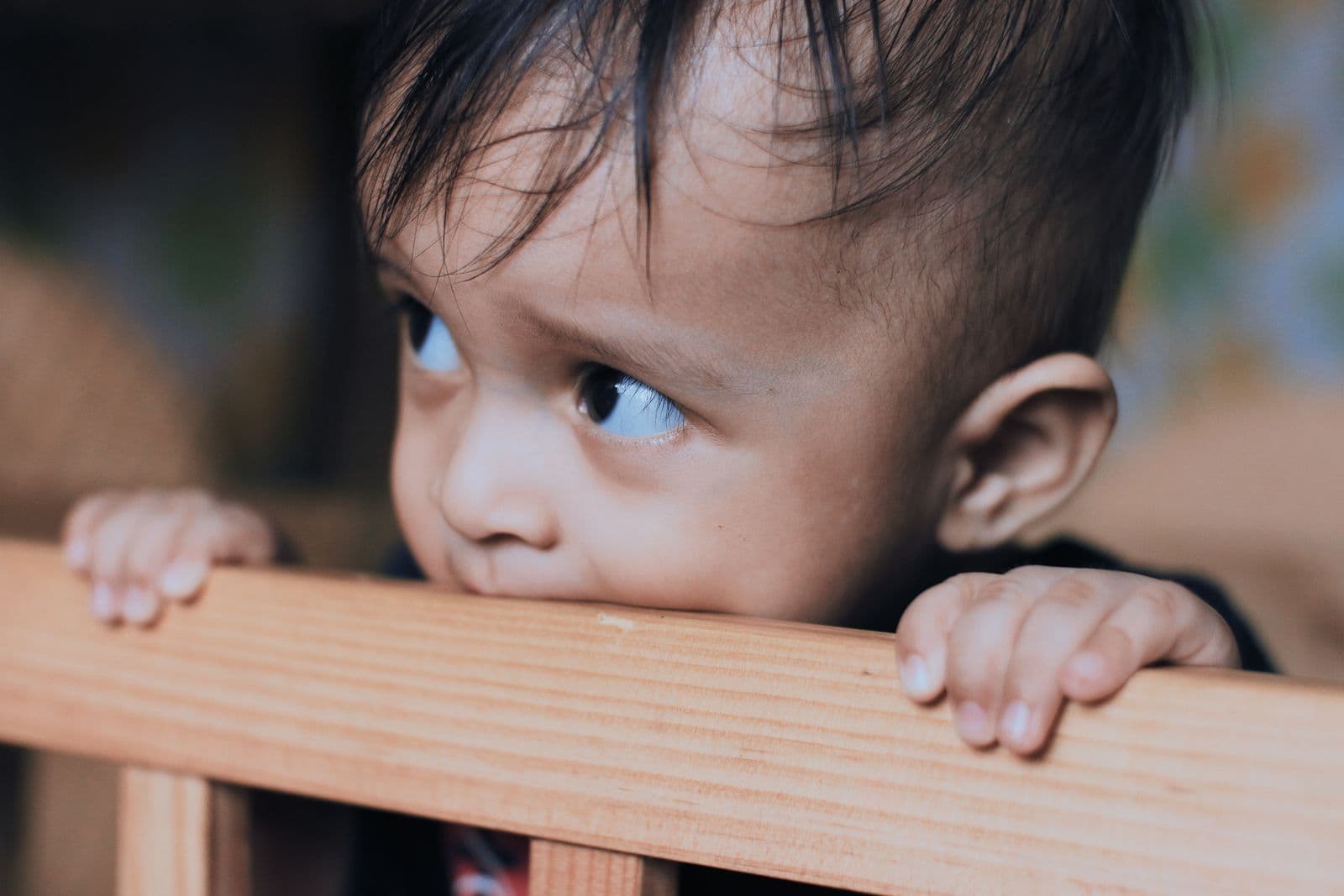 A baby gripping a wooden rail with their teeth and hands, mid-bite