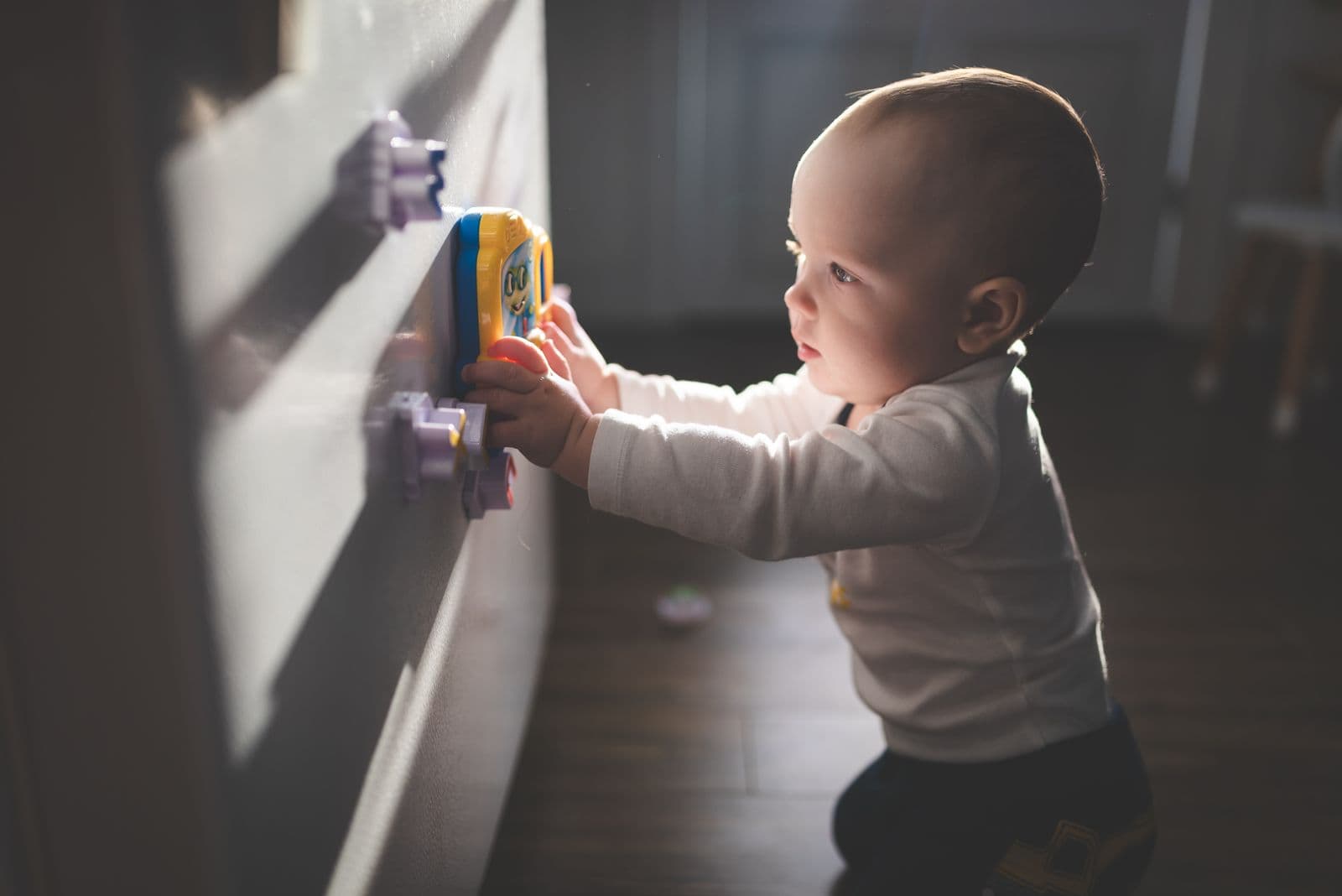 A baby standing at a cupboard, pressing colourful magnetic toy pieces against the door