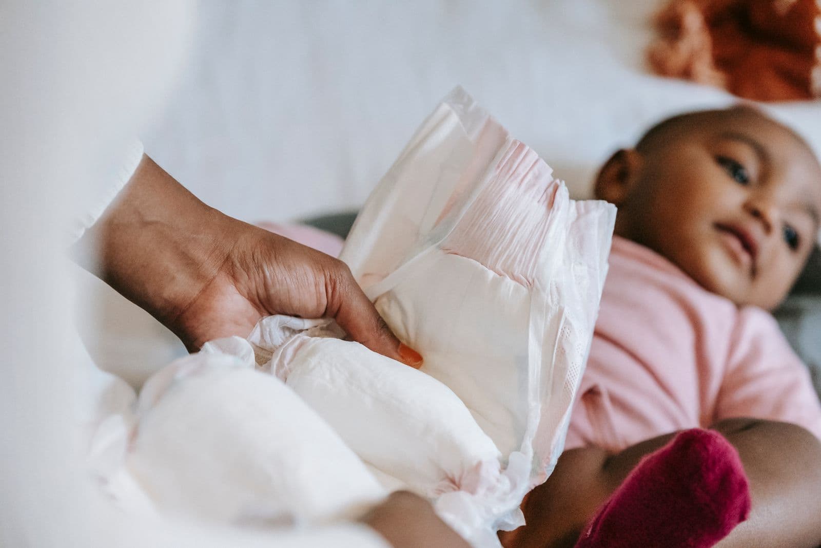 A parent holding a clean diaper beside a baby lying on her back on a changing surface