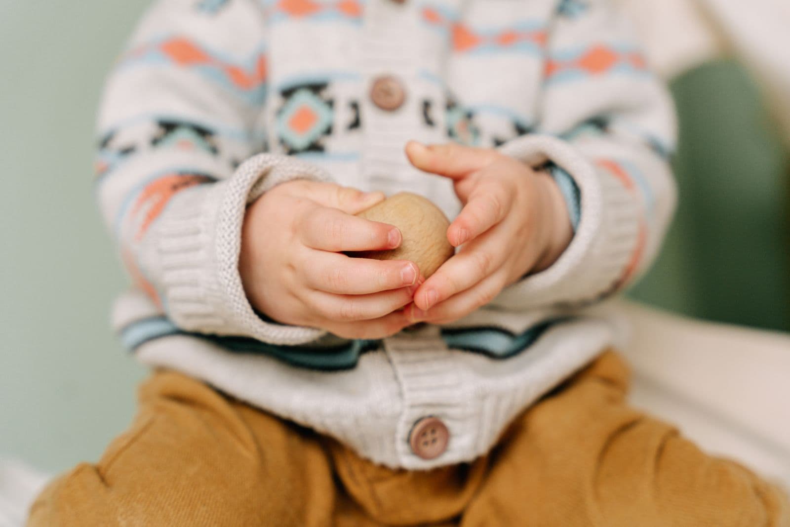 A toddler's hands holding a small round wooden object
