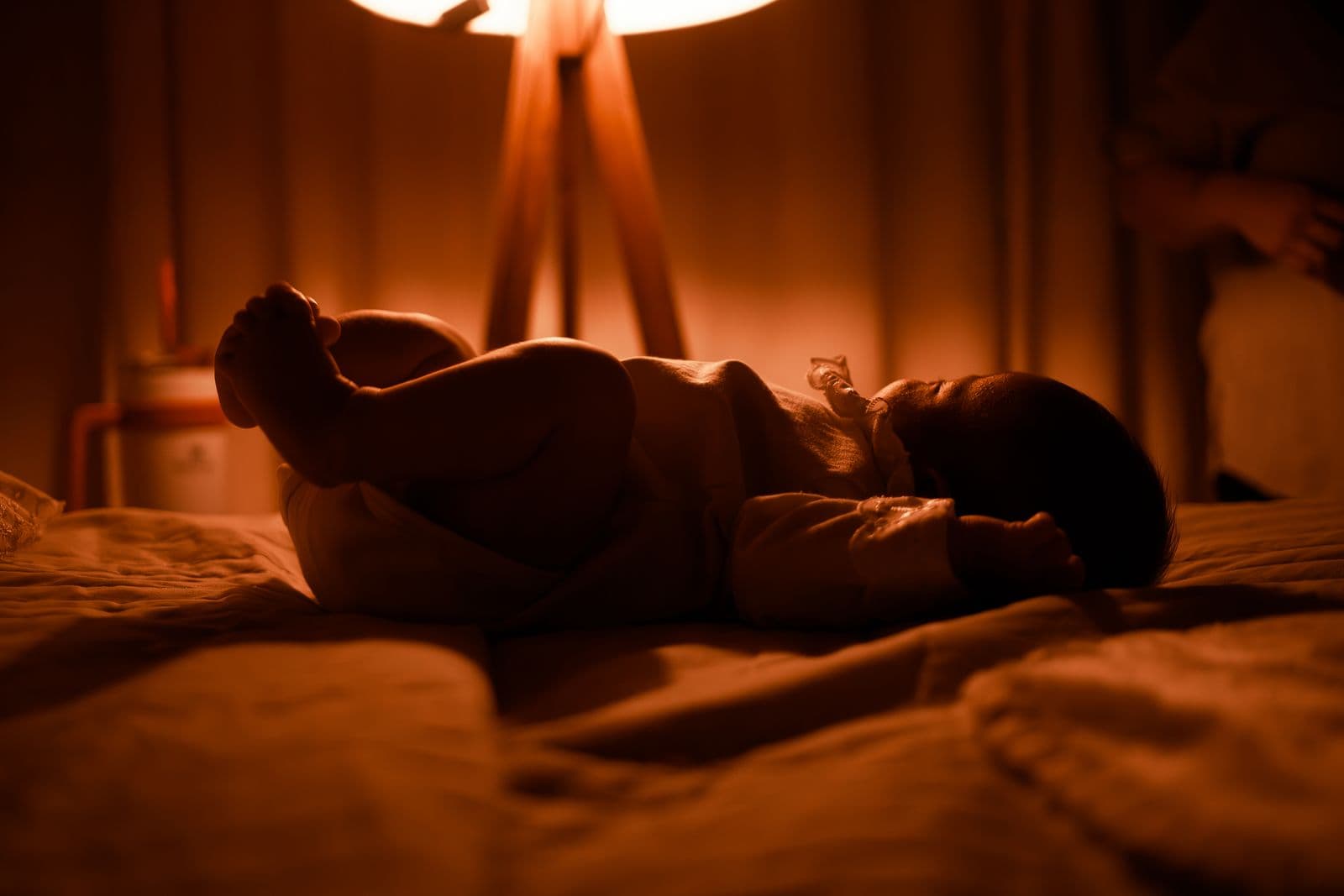 A baby asleep on a bed in warm lamplight