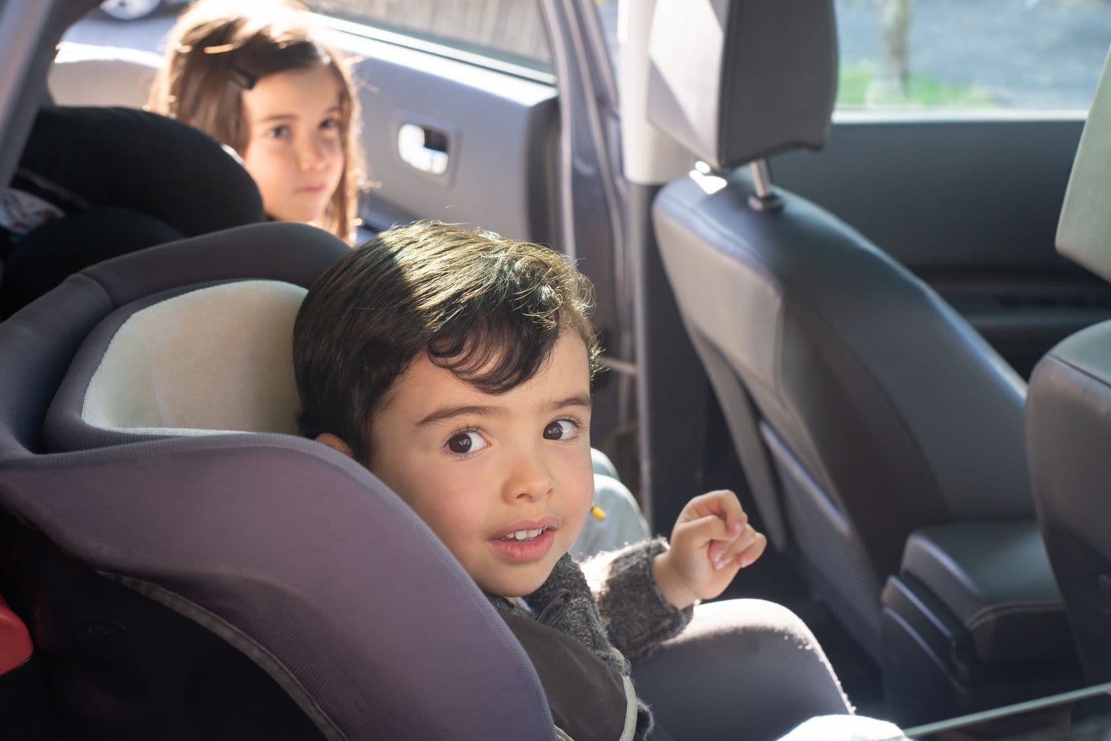 Two children sitting in car seats in the back of a car
