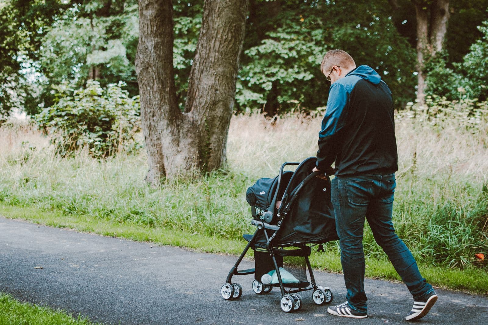 A parent walking a baby in a stroller along a path through a wooded park