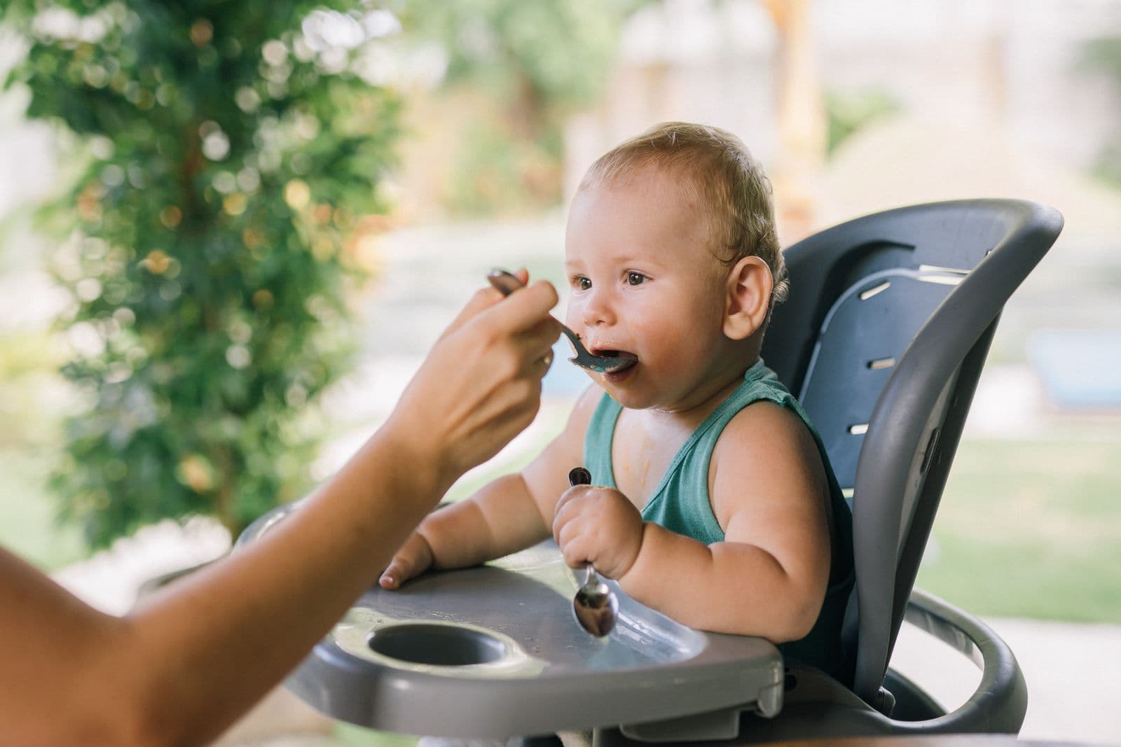 A parent spoon-feeding a baby seated in a high chair