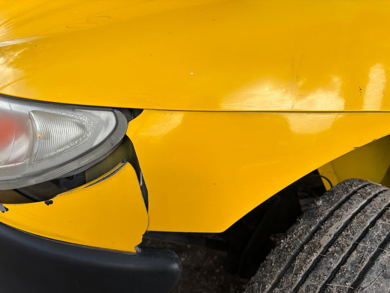 Close-up of a yellow car's cracked front bumper beside the headlight after a collision