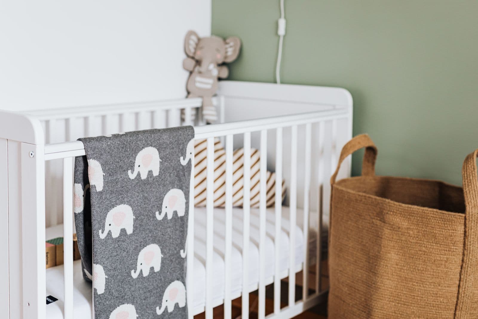 A white wooden crib with a knitted blanket hanging over the side rail