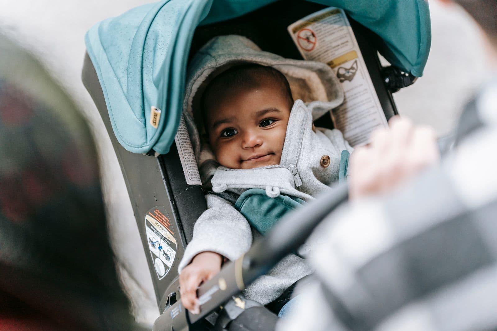 A baby looking up from a stroller seat while a parent adjusts the harness
