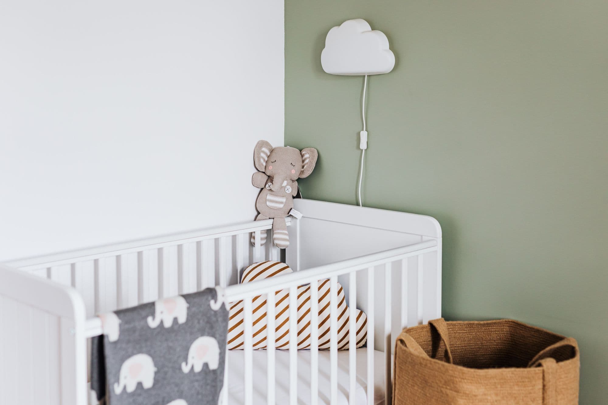 A calm nursery corner: a light oak crib with a muslin blanket over the rail, an oak dresser and a vase of branches